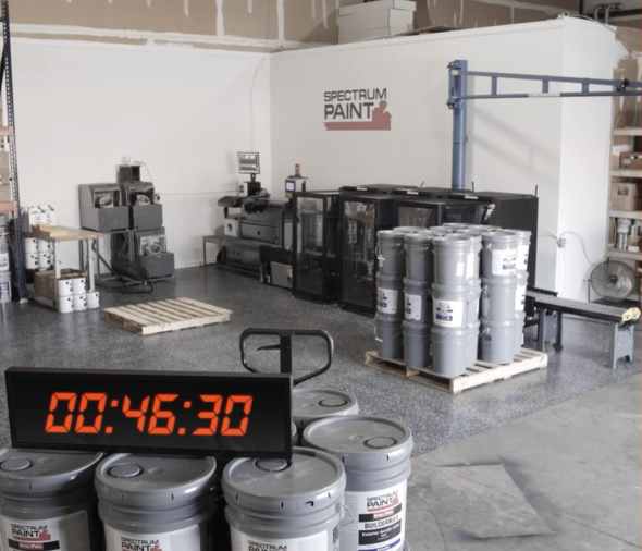 Automated paint mixing system at Spectrum Paint facility with stacked paint buckets and a digital timer reading 00:46:30, highlighting the speed and efficiency of the automation process.